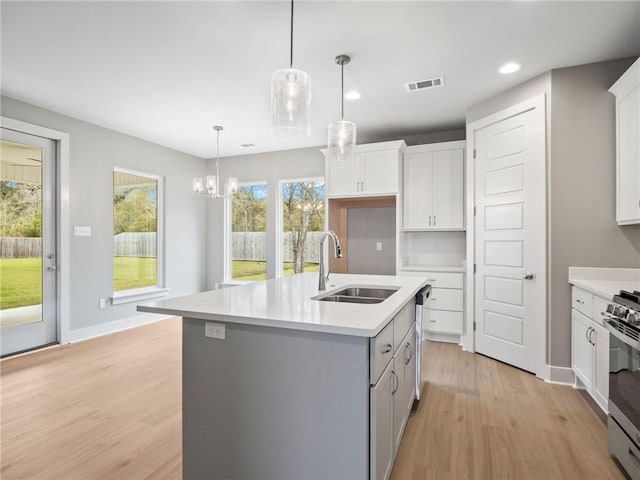 kitchen featuring an island with sink, light hardwood / wood-style floors, decorative light fixtures, and sink