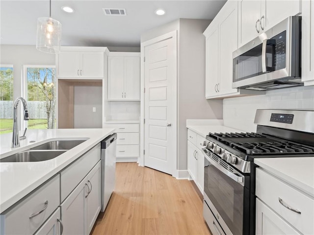 kitchen with light hardwood / wood-style floors, white cabinets, stainless steel appliances, sink, and hanging light fixtures