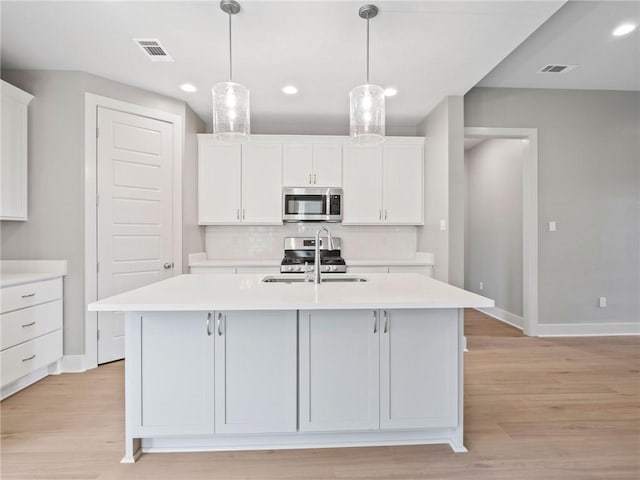 kitchen featuring appliances with stainless steel finishes, a kitchen island with sink, light wood-type flooring, and white cabinetry