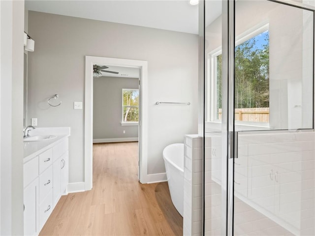 bathroom with shower with separate bathtub, ceiling fan, vanity, and wood-type flooring