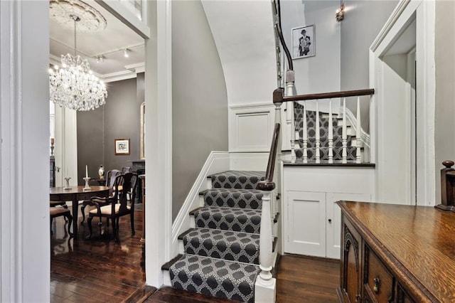 stairs featuring dark hardwood / wood-style flooring, track lighting, and an inviting chandelier