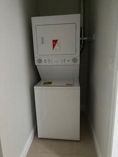 clothes washing area featuring stacked washing maching and dryer and light tile floors