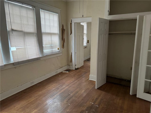 unfurnished bedroom featuring dark wood-type flooring, multiple windows, and a closet