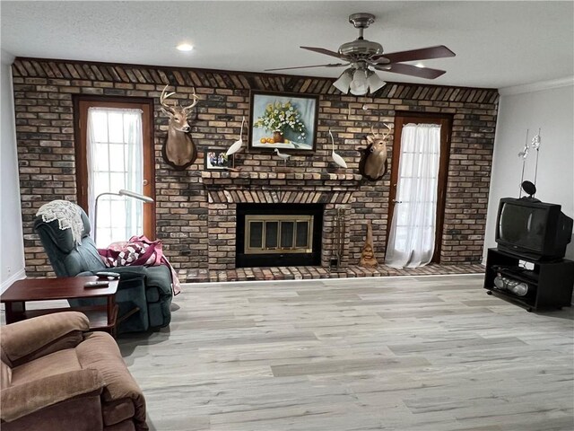 living room with brick wall, a brick fireplace, ceiling fan, light hardwood / wood-style flooring, and a textured ceiling