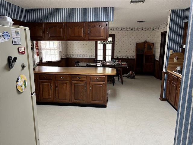 kitchen with dark brown cabinetry, white fridge, a textured ceiling, and kitchen peninsula