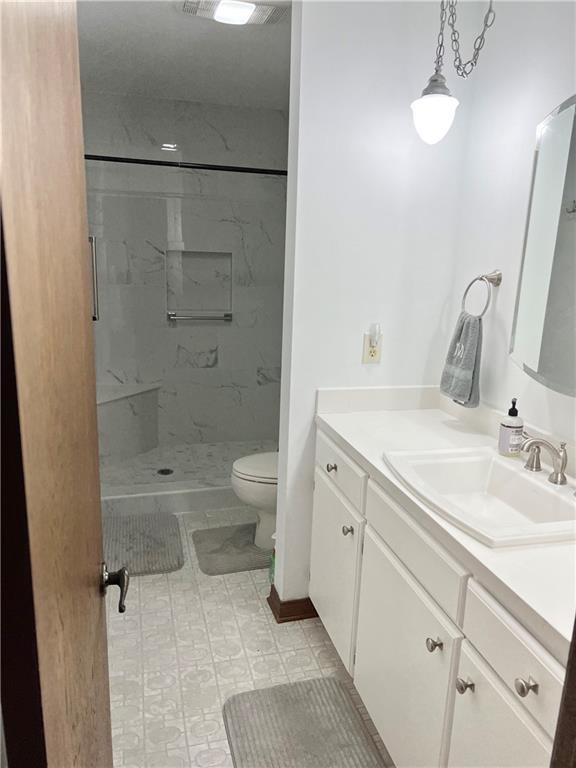 bathroom with vanity, tiled shower, and toilet