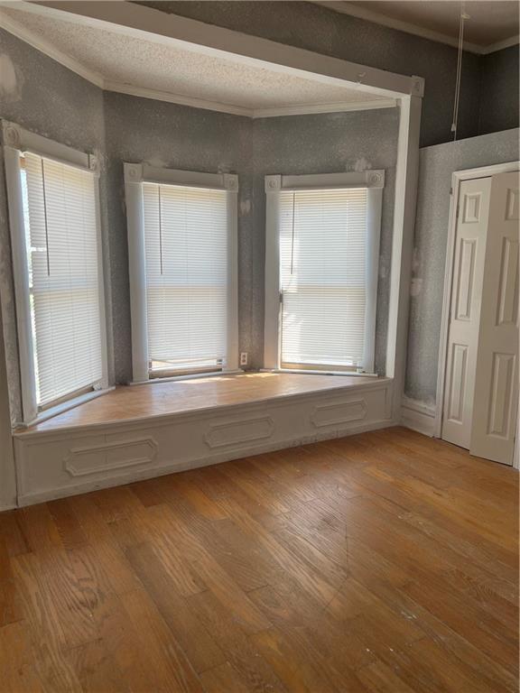 empty room with a wealth of natural light, ornamental molding, and light wood-type flooring