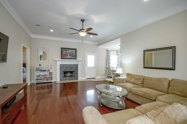 living room with ornamental molding, ceiling fan, hardwood / wood-style flooring, and a tiled fireplace