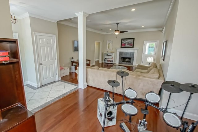 interior space with light tile flooring, ceiling fan, a tiled fireplace, crown molding, and decorative columns