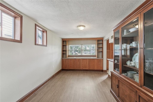 empty room featuring built in features, light hardwood / wood-style floors, and a textured ceiling