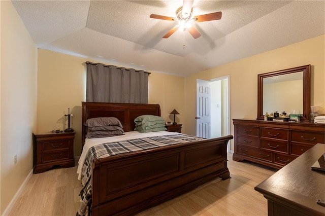 bedroom with a raised ceiling, light hardwood / wood-style floors, a textured ceiling, and ceiling fan