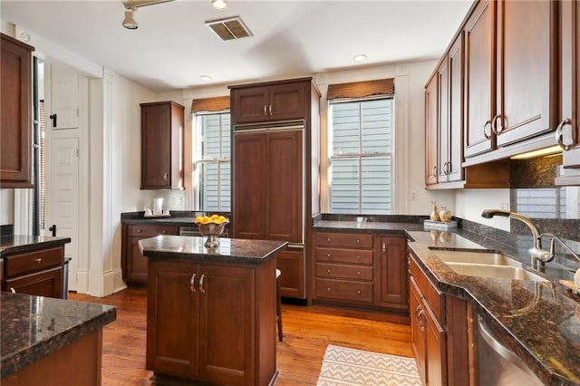 kitchen with dark stone counters, paneled built in refrigerator, a center island, hardwood / wood-style floors, and sink