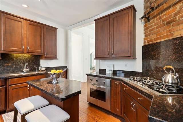 kitchen with a kitchen bar, dark stone countertops, stainless steel appliances, hardwood / wood-style floors, and sink