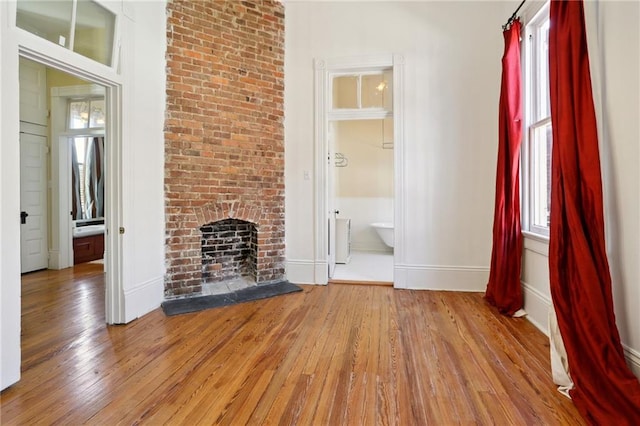 unfurnished living room with a fireplace, brick wall, and light wood-type flooring