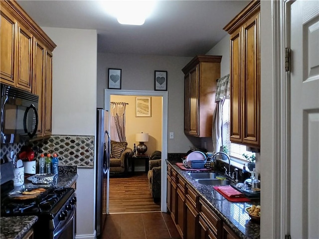 kitchen with black appliances, dark tile patterned flooring, sink, decorative backsplash, and dark stone countertops