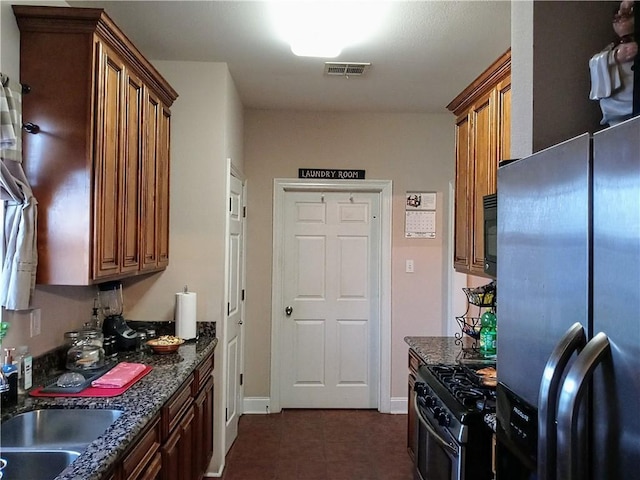 kitchen featuring appliances with stainless steel finishes, dark tile patterned flooring, dark stone counters, and sink