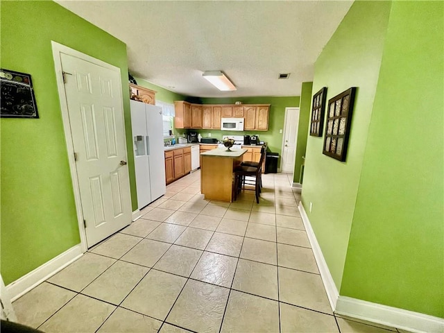 kitchen with white appliances, light tile patterned flooring, a breakfast bar area, and a kitchen island