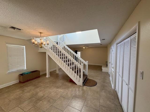 interior space featuring a skylight, a textured ceiling, a notable chandelier, and light tile floors