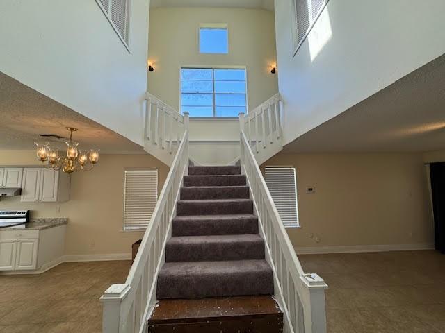 stairs featuring an inviting chandelier, dark tile floors, and a towering ceiling