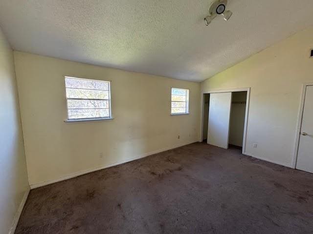 unfurnished bedroom featuring a closet, a textured ceiling, dark colored carpet, and vaulted ceiling