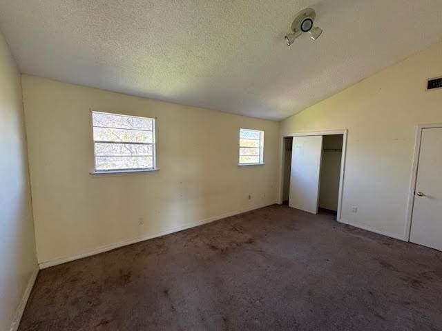 unfurnished bedroom featuring a textured ceiling, a closet, dark colored carpet, and lofted ceiling