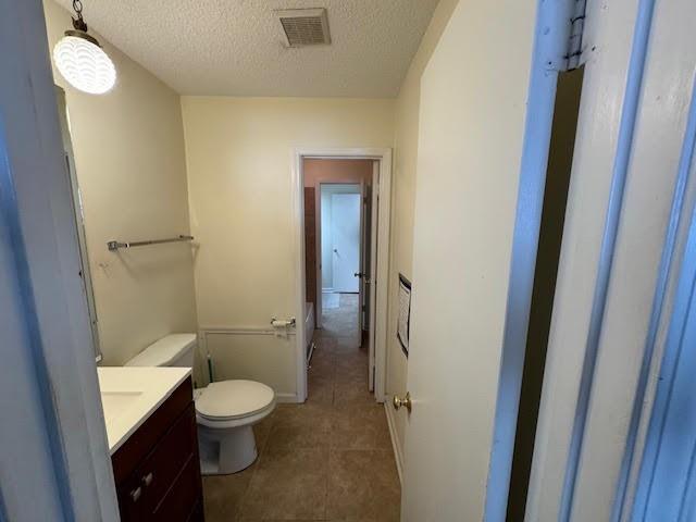 bathroom with toilet, a textured ceiling, vanity, and tile flooring