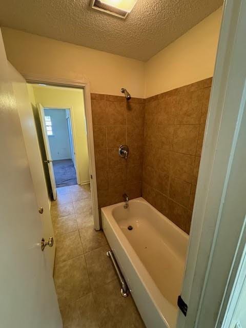 bathroom with tile flooring, tiled shower / bath combo, and a textured ceiling