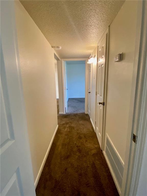 corridor featuring a textured ceiling and dark carpet