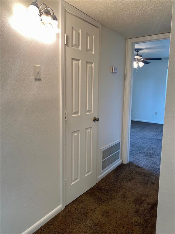 corridor featuring a textured ceiling, a chandelier, and dark colored carpet