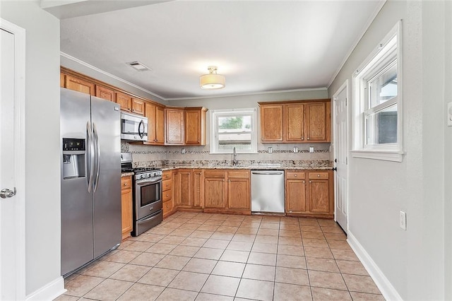 kitchen featuring sink, ornamental molding, appliances with stainless steel finishes, light tile flooring, and light stone countertops