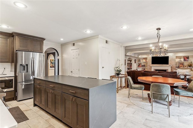 kitchen featuring dark brown cabinetry, a center island, stainless steel appliances, a large fireplace, and light tile patterned floors