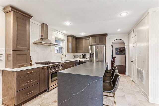 kitchen with a kitchen bar, appliances with stainless steel finishes, sink, a kitchen island, and wall chimney exhaust hood