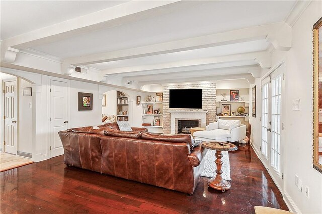 living room with built in shelves, dark hardwood / wood-style flooring, beamed ceiling, a fireplace, and ornamental molding