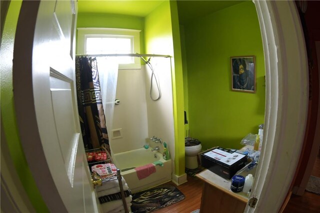 bathroom with washtub / shower combination, hardwood / wood-style flooring, and toilet