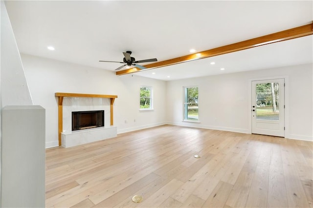 unfurnished living room with light hardwood / wood-style flooring, a premium fireplace, beam ceiling, and ceiling fan