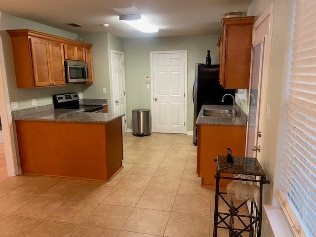 kitchen featuring appliances with stainless steel finishes, dark stone countertops, a kitchen bar, light tile floors, and sink