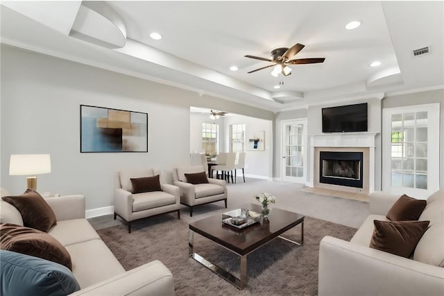 carpeted living room with a tray ceiling, plenty of natural light, a tile fireplace, and ceiling fan