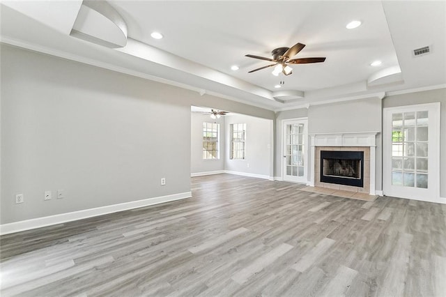 unfurnished living room featuring ceiling fan, a fireplace, a tray ceiling, and light hardwood / wood-style flooring