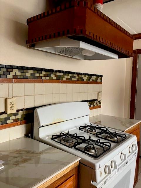 kitchen featuring exhaust hood, white gas range, and tasteful backsplash