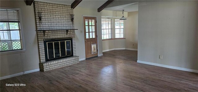 unfurnished living room with dark hardwood / wood-style flooring, beam ceiling, a brick fireplace, and a healthy amount of sunlight