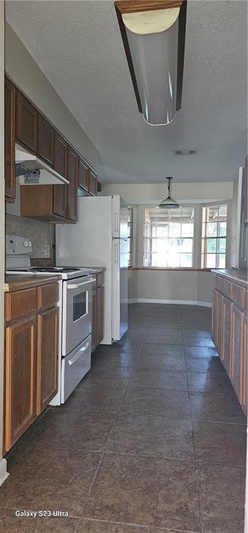 kitchen featuring a textured ceiling, tasteful backsplash, dark tile patterned flooring, and stainless steel electric range oven