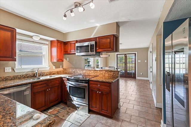 kitchen with track lighting, stainless steel appliances, dark stone countertops, kitchen peninsula, and french doors