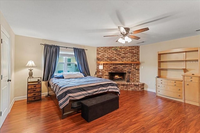 bedroom with dark hardwood / wood-style flooring, a fireplace, brick wall, and ceiling fan