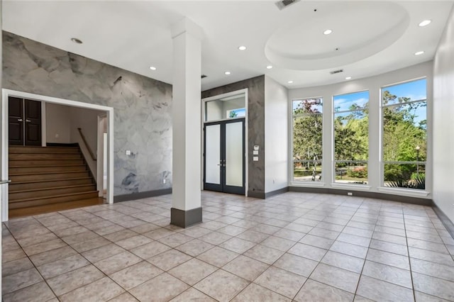 interior space with a healthy amount of sunlight, a tray ceiling, light hardwood / wood-style floors, and french doors