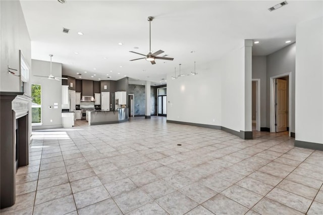 unfurnished living room with a high ceiling, ceiling fan, and light tile flooring