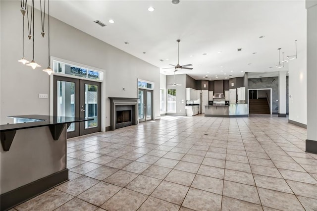 unfurnished living room featuring light tile floors, ceiling fan, a premium fireplace, and french doors