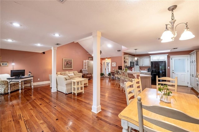 dining space featuring hardwood / wood-style floors, vaulted ceiling, and an inviting chandelier