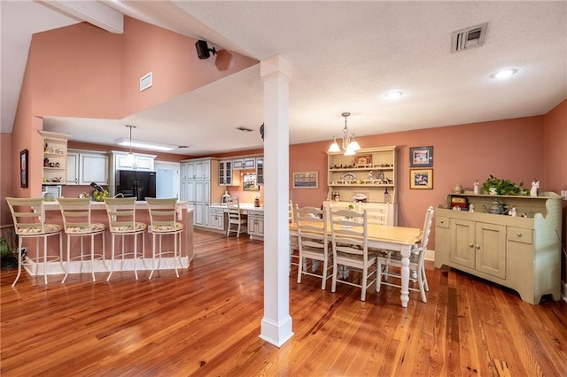 dining area with ornate columns, light hardwood / wood-style flooring, vaulted ceiling, and an inviting chandelier