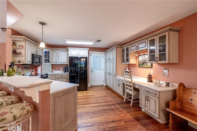 kitchen featuring black appliances, light hardwood / wood-style flooring, decorative light fixtures, kitchen peninsula, and a breakfast bar area