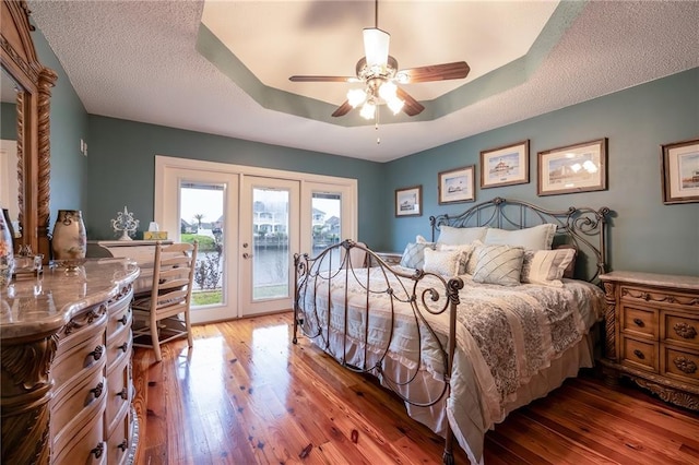 bedroom with hardwood / wood-style floors, access to outside, french doors, ceiling fan, and a tray ceiling